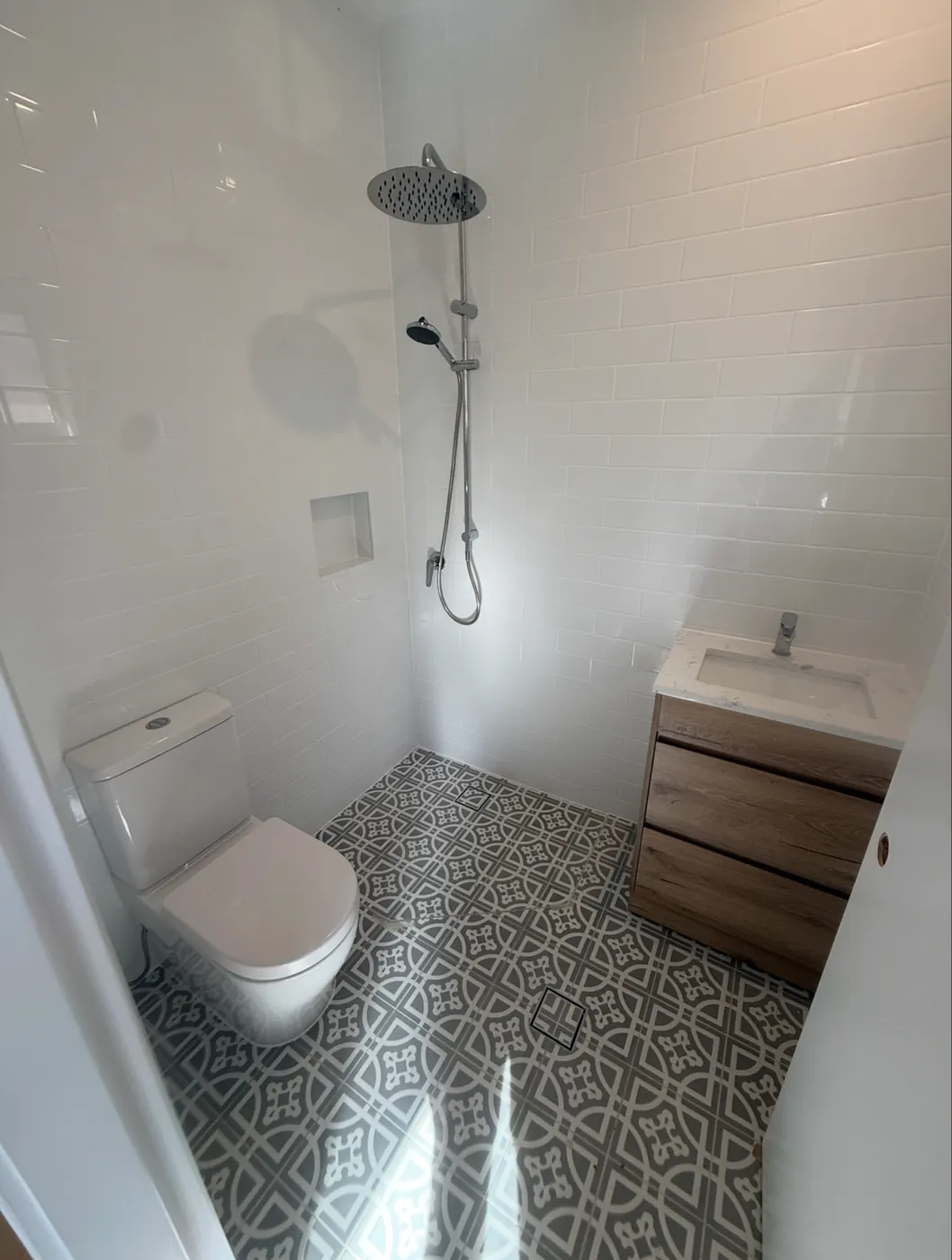 Small bathroom with a toilet, timber vanity and patterned floor tiles