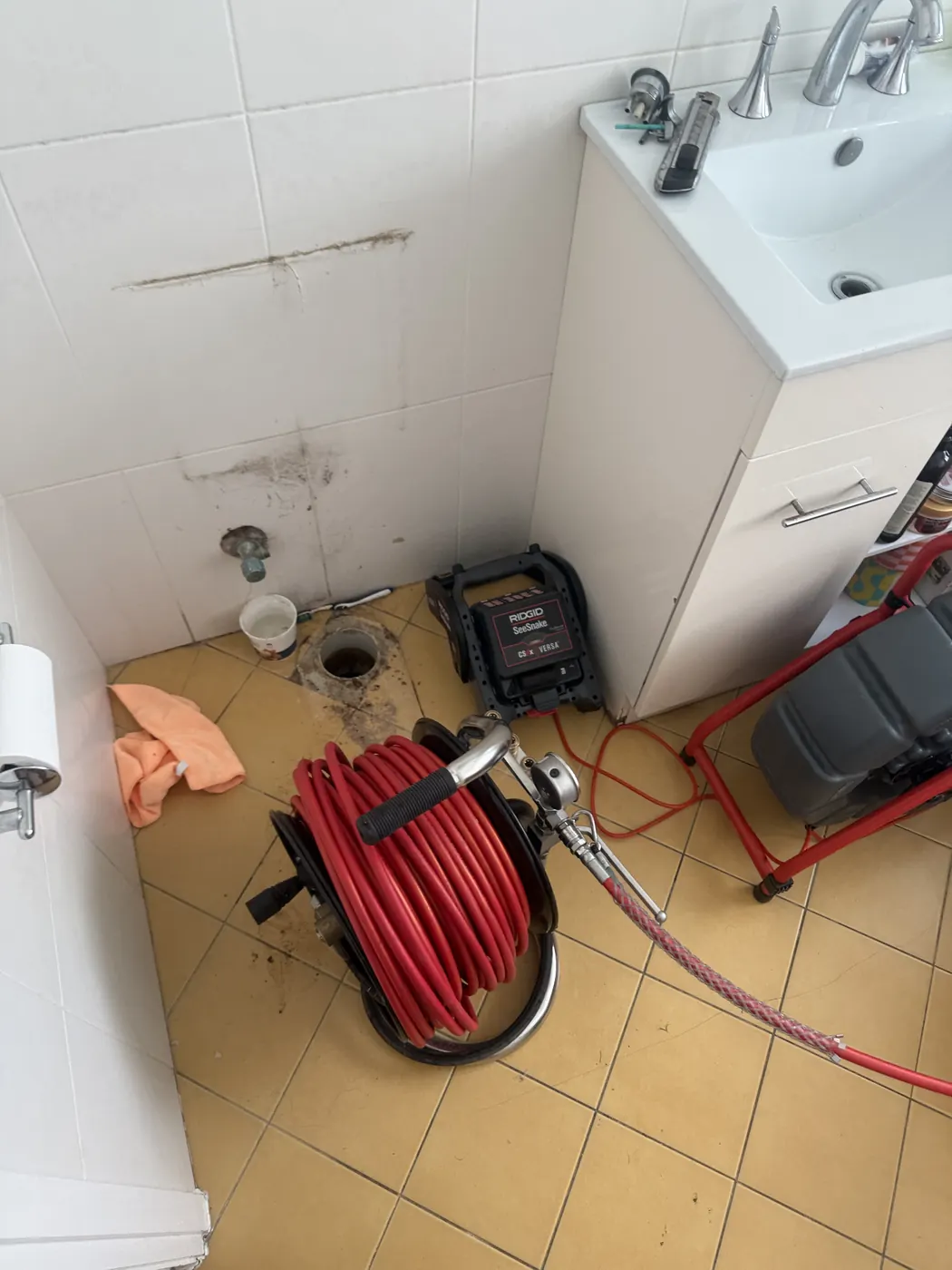 Drain camera and jet blaster set up in a bathroom with the toilet removed