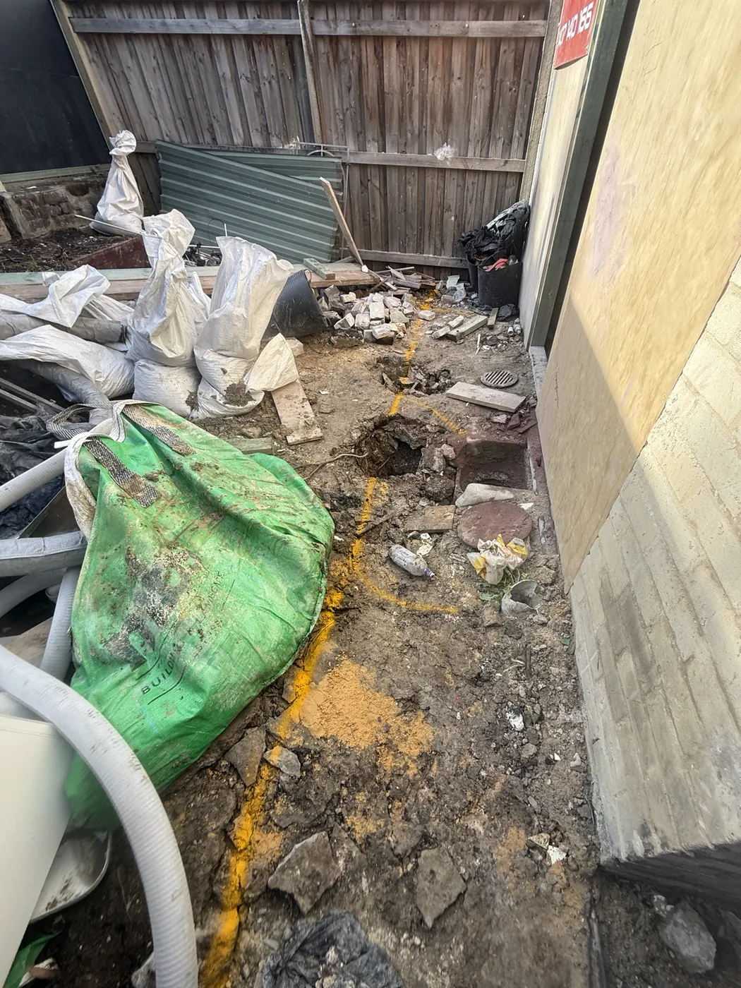 Side path dug up during a drain repair, with bags of spoil and pipe