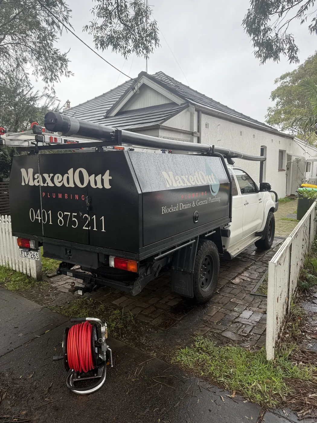 Jet blaster hose reel on the footpath behind the signwritten MaxedOut ute