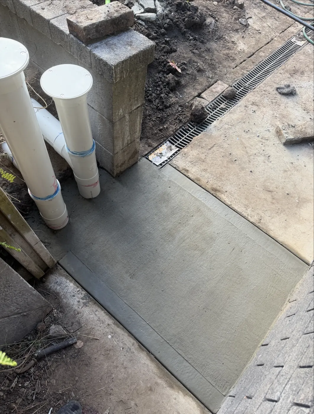 New PVC risers and fresh concrete beside a strip drain