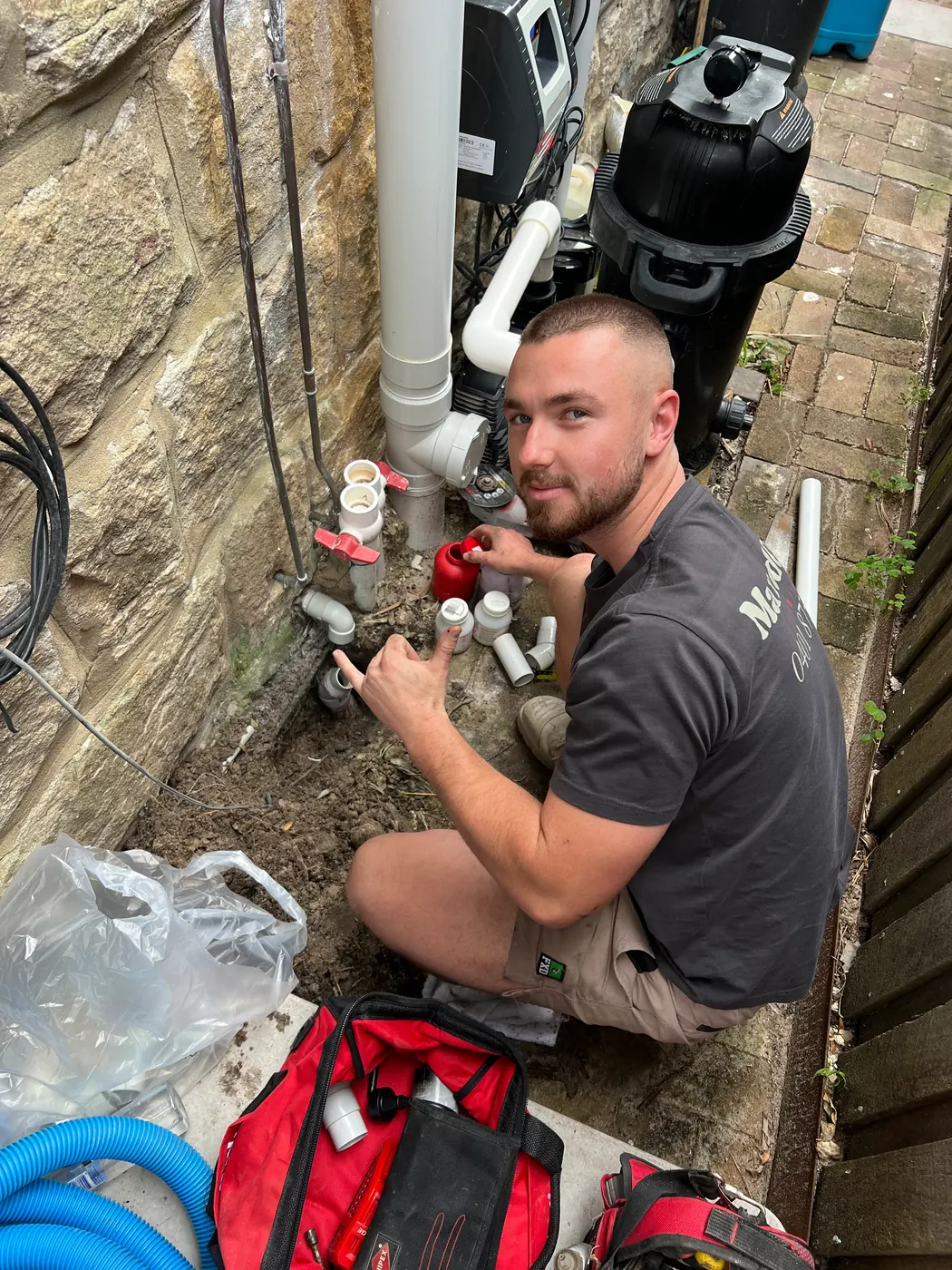 MaxedOut plumber working on pipework at a water meter beside a sandstone wall