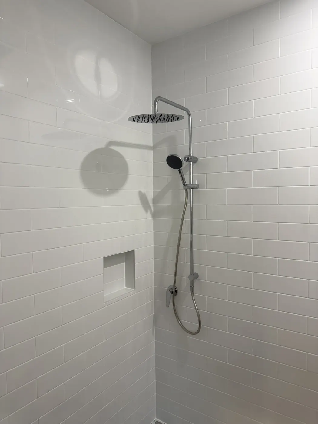 Shower rail and mixer on white subway tiles with a niche