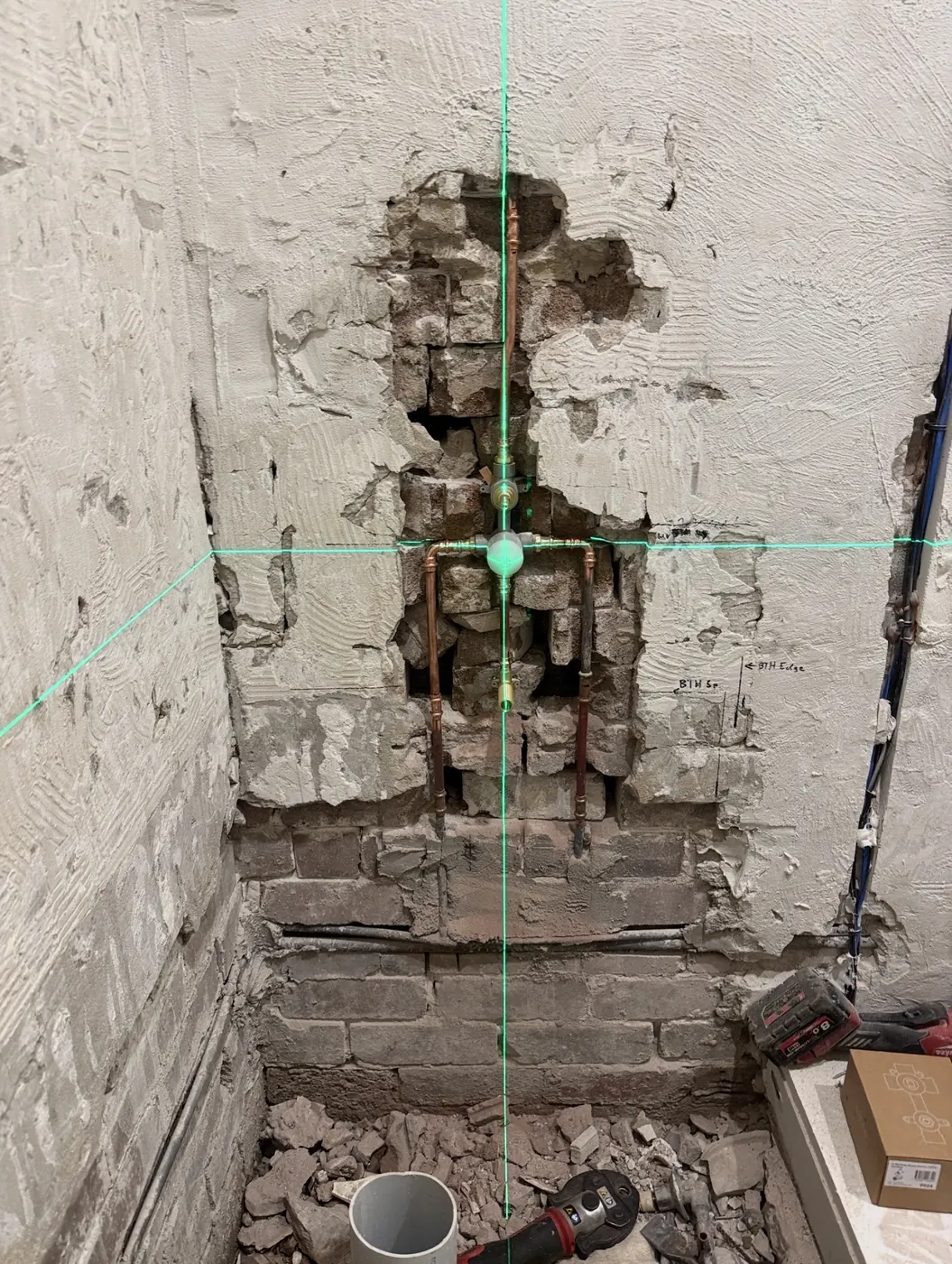 Shower wall opened up to the pipework for a new mixer tap, with a laser level line across it