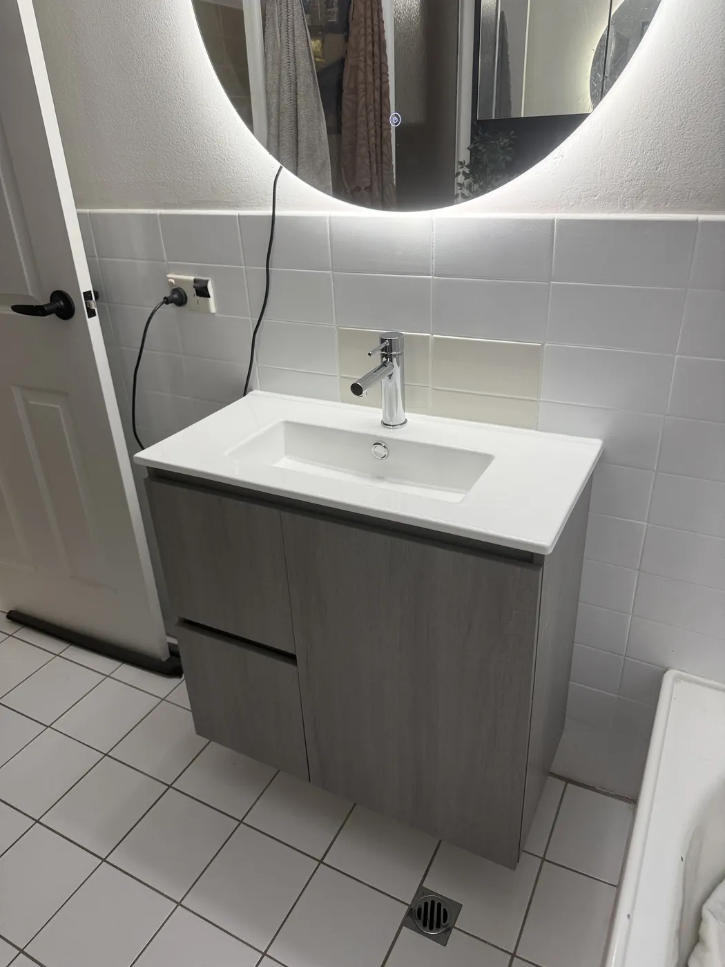 Vanity with a chrome mixer under a round backlit mirror